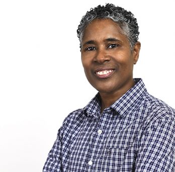 an African-American person with short hair and a checked shirt smiles while facing forward 