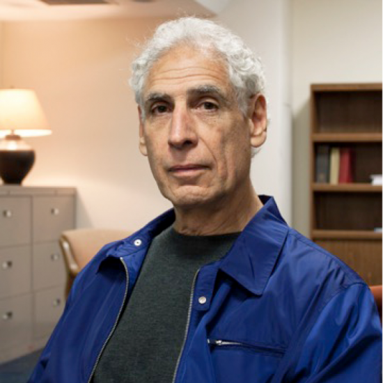 man in blue jacket and grey shirt and short hair looks at the camera