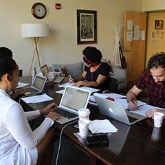 a small group of individuals sits around a table with laptops in front of them