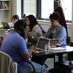 a small group of individuals sits around a table with laptops in front of them