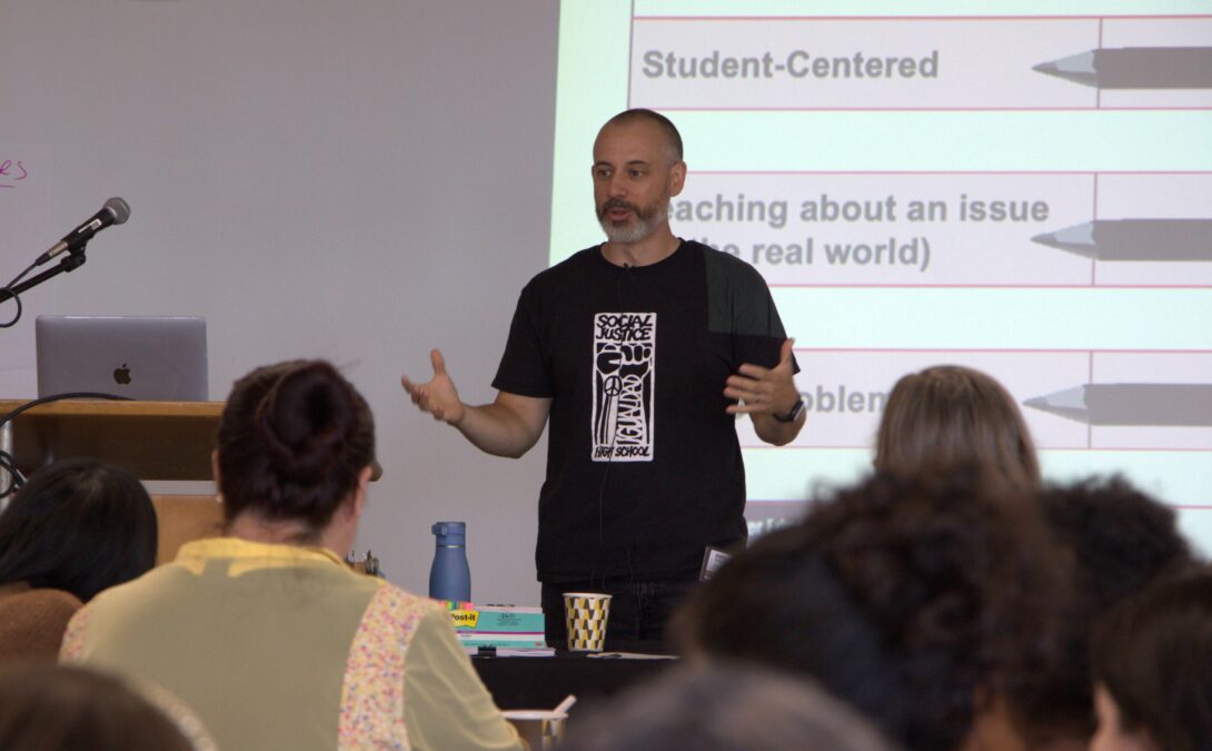 A person gestures to a group of people while standing at the front of the room.