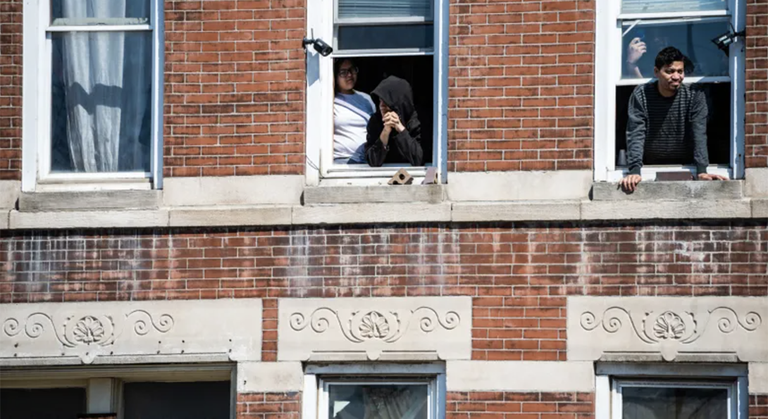 A photograph of people in Pilsen standing at their windows looking out into the street