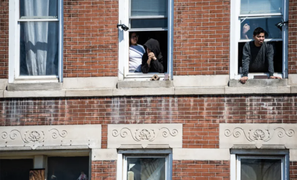 A photograph of people in Pilsen standing at their windows looking out into the street